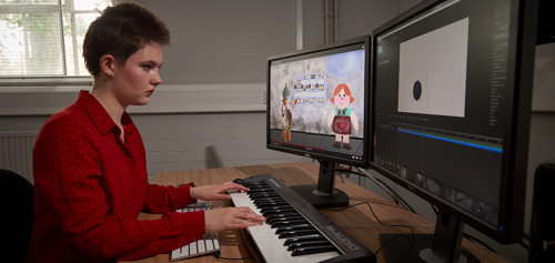 Student sitting in front of a dual screen desktop playing a keyboard