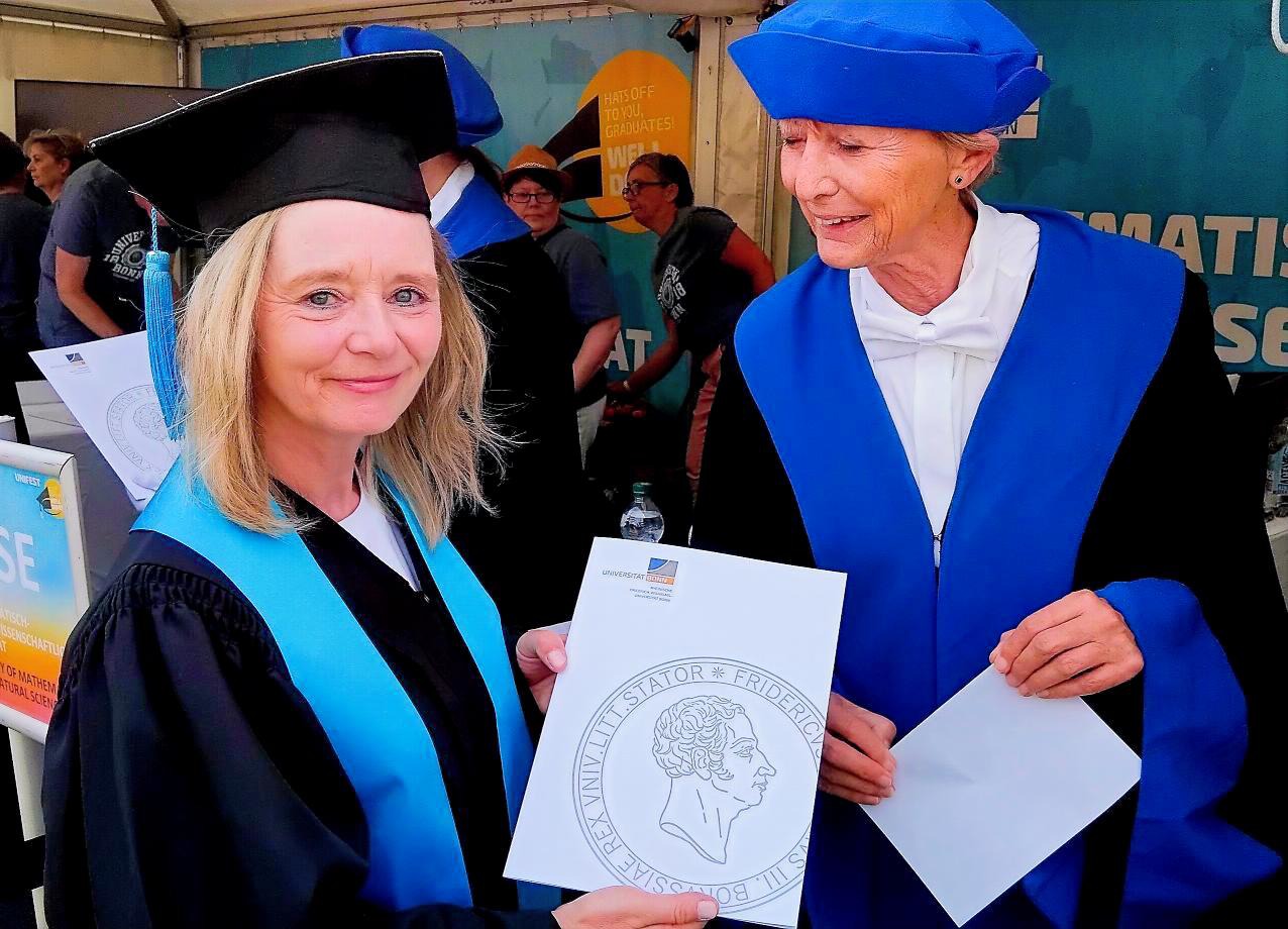 Graduate posing with her diploma in front of a provost 